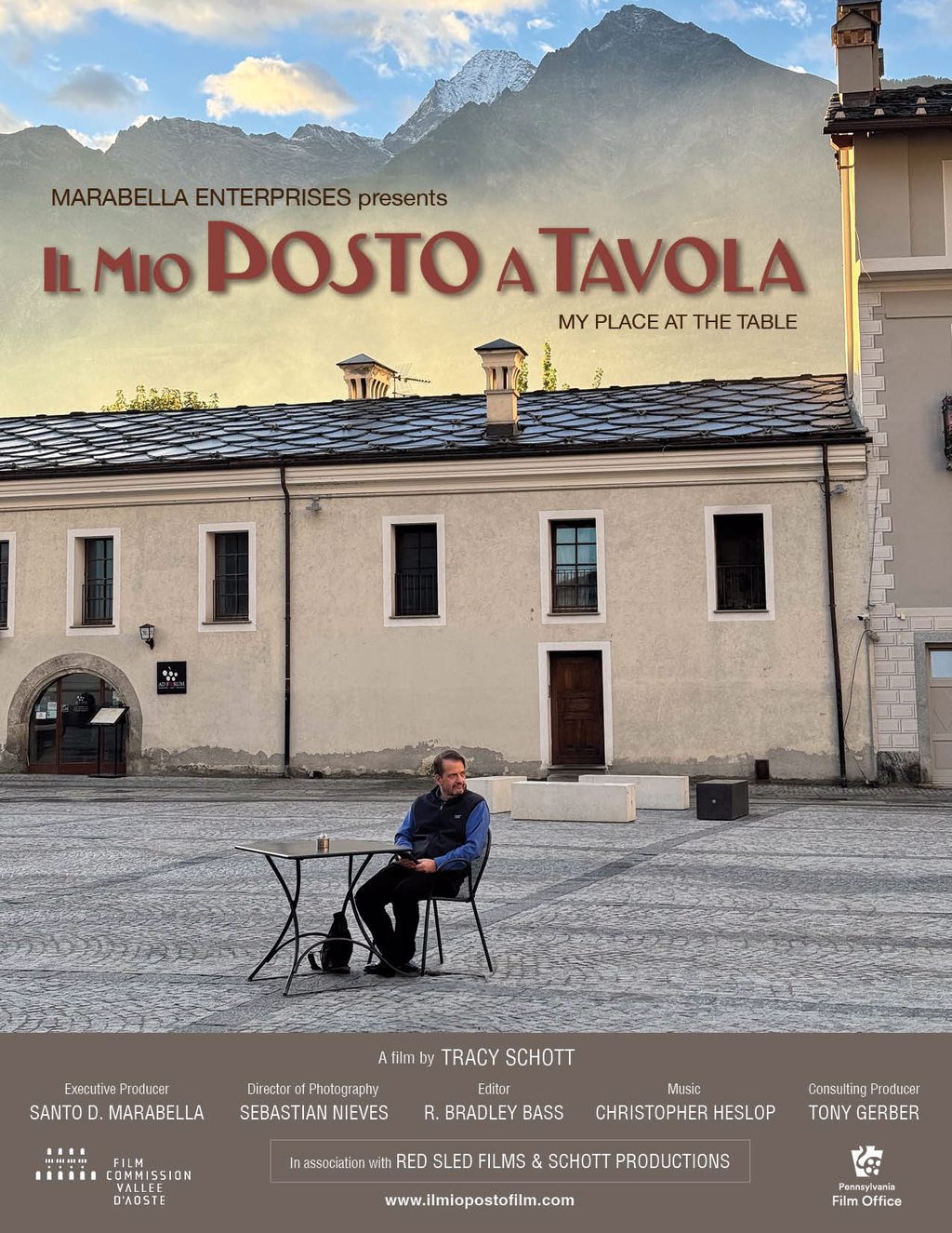 POSTER FOR IL MIO POSTO A TAVOLA (MY PLACE AT THE TABLE) FEATURING A MOUNTAIN SKY IN THE BACKGROUND WITH A HOME AND A MAN SITTING AT A TABLE IN THE ONLY CHAIR IN FRONT OF THE HOUSE